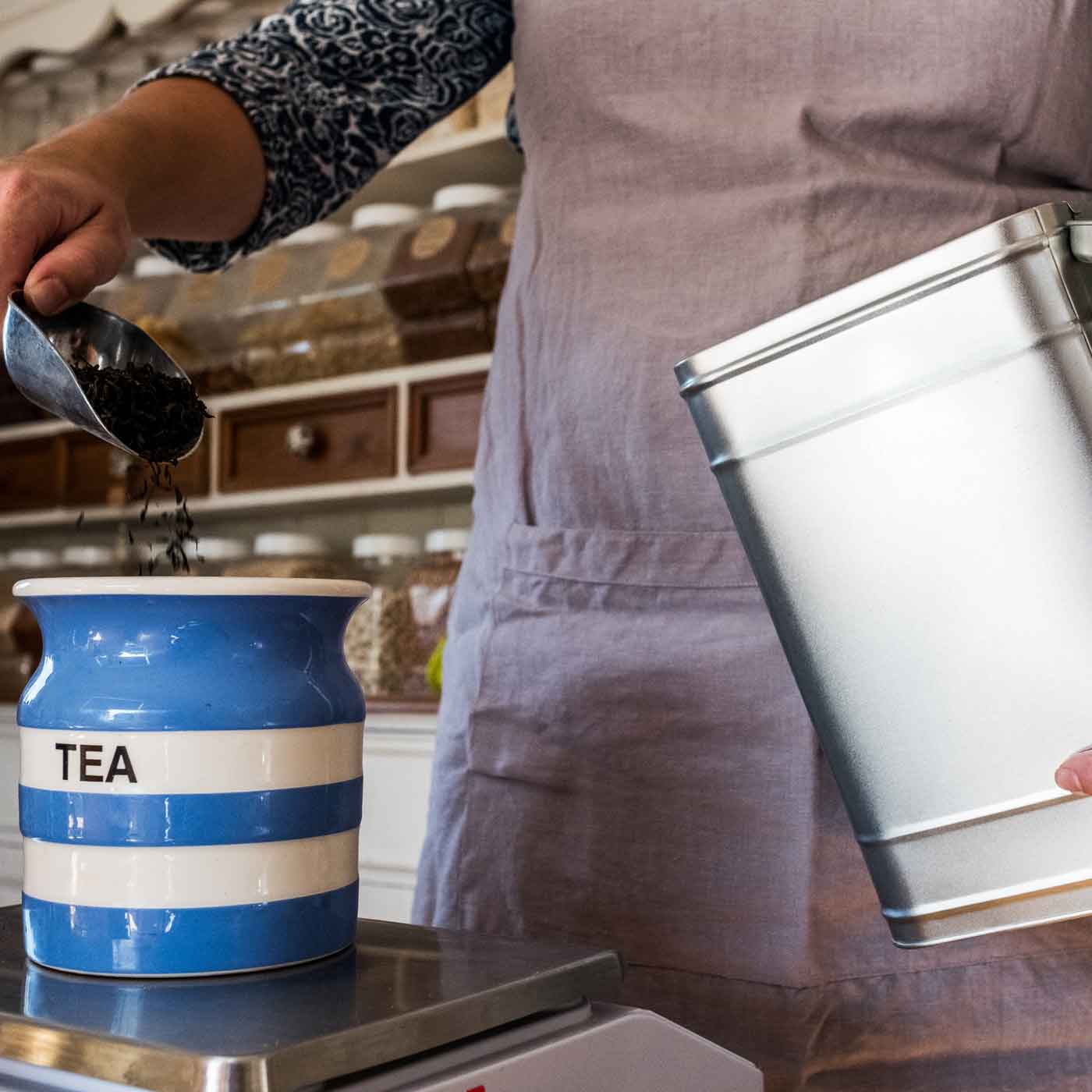 Frau füllt Tee von einer silbernen Vorratsdose in ein Keramikgefaess Fun Fact Produkt Vorratsdosen verschiedene Designs & Farben online kaufen bei Genussio